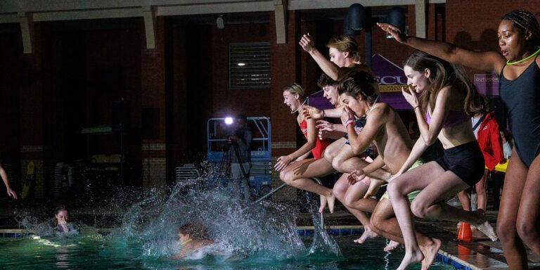 A group of students jumping into a swimming pool at night, making splashes