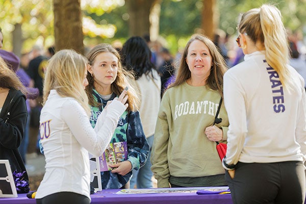 : mother and daughter speak to E C U staff members tabling at Open House