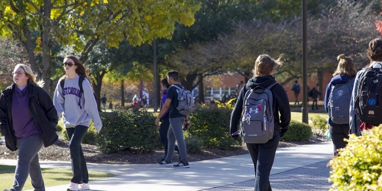 Students walk among the fall leaves by the Rawl Building on the E C U campus