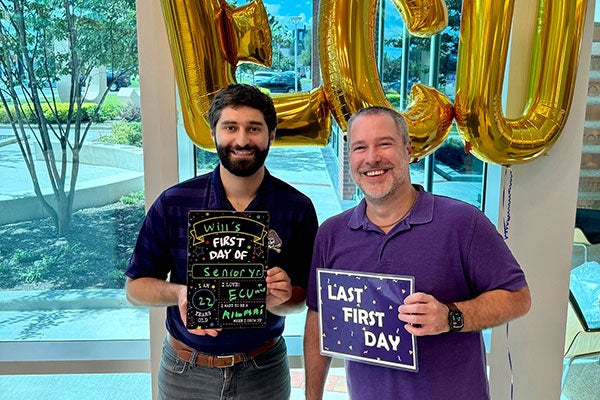 two males pose in front of gold E C U balloons with “First Day of Class” signs.