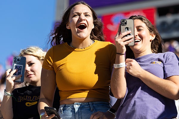 Three female students cheer on the Pirates an ECU Homecoming football game.